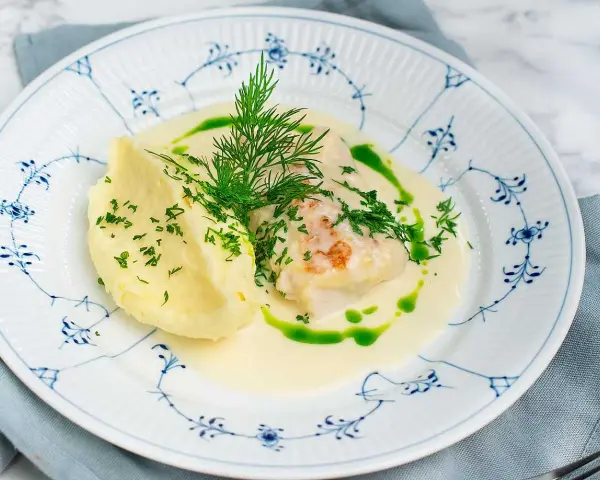 En vacker tallrik med torsk i en krämig sås, serverad med potatismos och dill. Ett perfekt torsk recept för en festmåltid.