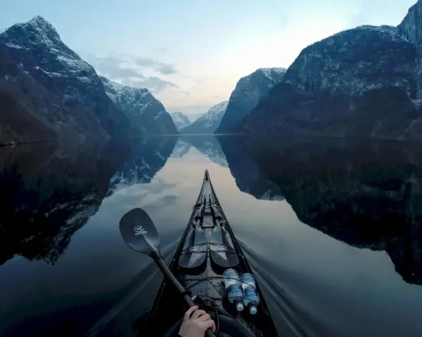 Kajakpaddling i en norsk fjord med snöklädda berg som speglar sig i det lugna vattnet. En fantastisk utsikt över son Norge.