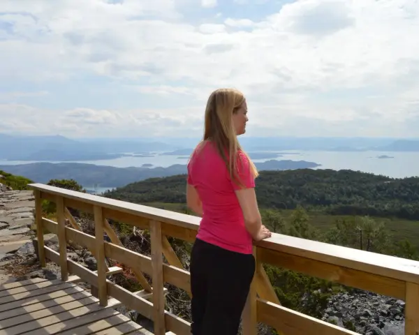 Kvinna i rosa tröja njuter av utsikten över ett storslaget Norge med fjäll och fjordar.