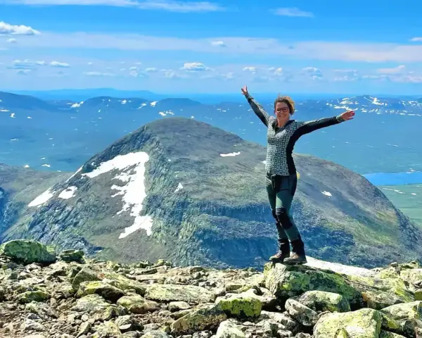 Lycklig vandrare på en bergstopp med vidsträckt utsikt över fjällandskap. Här finns fina vandringsleder för alla.
