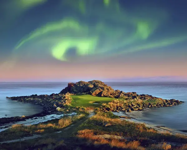 En unik golfbana i Norge under norrsken. En grönskande golfgreen omgiven av klippor och hav, med ett magiskt norrsken som lyser upp himlen.