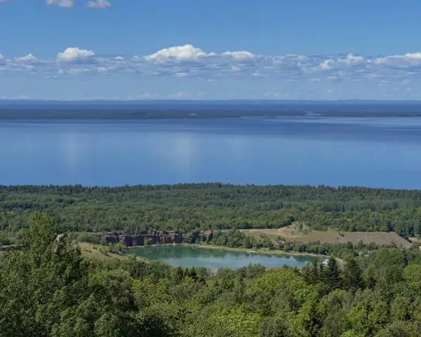 Vacker utsikt över en sjö och en grönskande skog. En liten sjö med klippor syns i mitten, en del av **Götaleden etapp 7**.