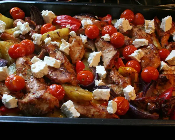 En härlig grekisk pyttipanna med kyckling, potatis, tomater, paprika och fetaost i en ugnsform.