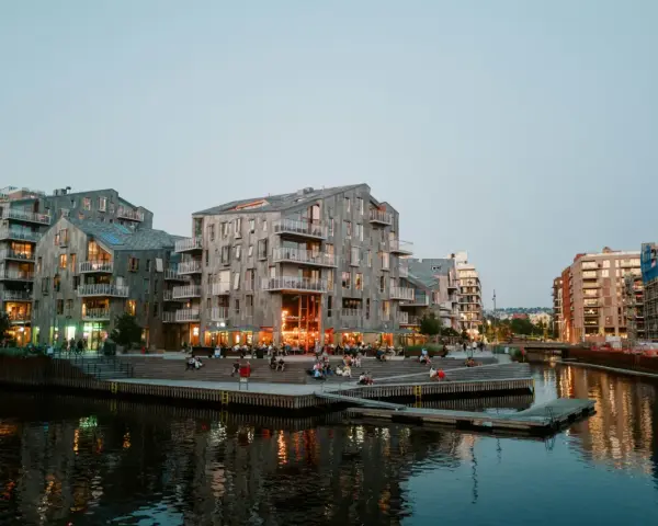 Moderna byggnader längs en kanal i Oslo. Folk sitter på trappor vid vattnet. Besök Oslo för en härlig kväll.
