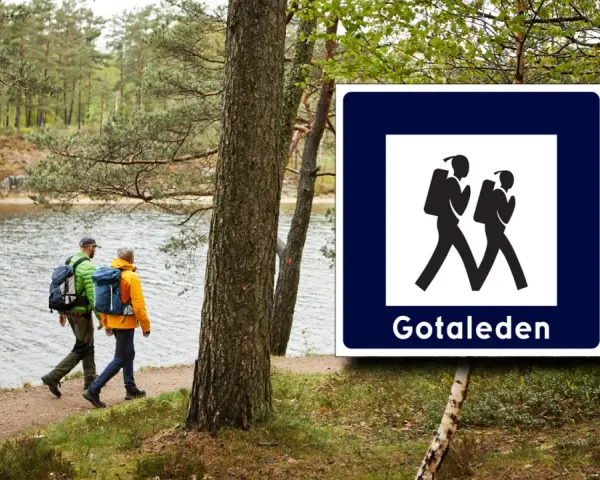 Två vandrare med ryggsäckar följer stigen längs en sjö. Skylt visar vandringsled Gotaleden etapp 6.