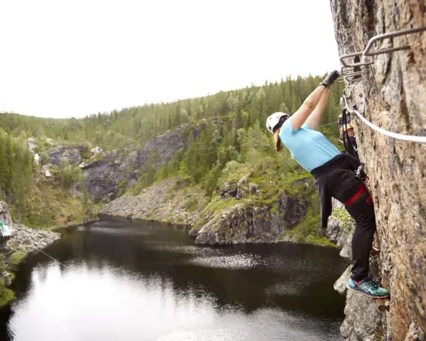 En person klättrar på en klippa vid rypetoppen adventurepark. Vacker natur med sjö och skog.