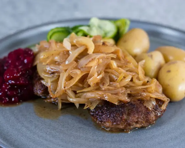 En tallrik med pannbiff, stekt lök, lingonsylt och kokt potatis. Ett klassiskt svenskt pannbiff recept som är lätt att lyckas med.