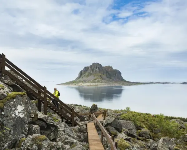 Vandrare på trappor vid havet med en imponerande bergstopp i bakgrunden, en vy från Vega Norge.