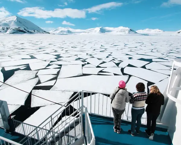 Besök Svalbard och se isflak som bryts upp i ett arktiskt landskap. Tre personer står på ett fartyg och blickar ut över det frusna havet.