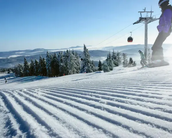 Perfekt preparerad pist för sommarskidåkning i Norge. En snowboardåkare och en skidåkare njuter av den soliga dagen.