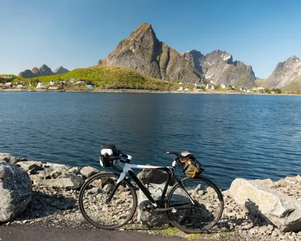 En cykel står vid en sjö med berg och en by i bakgrunden. Perfekt för mtb norge-äventyr.