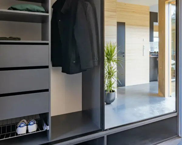 Snygga inredningstips hall: mörk garderob med rockar, mössor, skor och en grön växt som speglas i en stor glasdörr.