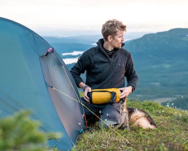Man med hund packar för vandring. En gul sovsäck ligger redo. Perfekt packlista vandring dagstur.