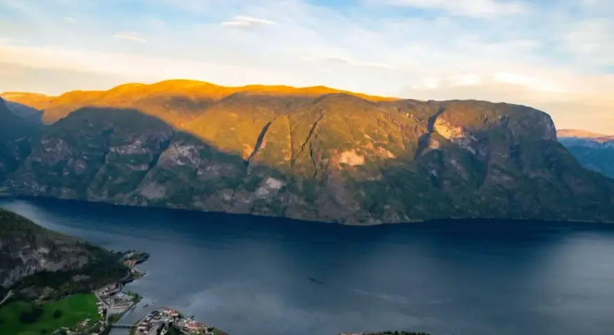 En vy över Sognefjorden med solbelysta berg och en liten by vid vattnet. Som en levande sognefjorden karta.