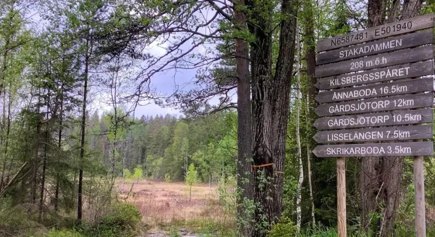 Skylt vid Kilsbergens vandringsled visar vägen till Stakadämmen och andra platser. En vacker skogsmiljö.