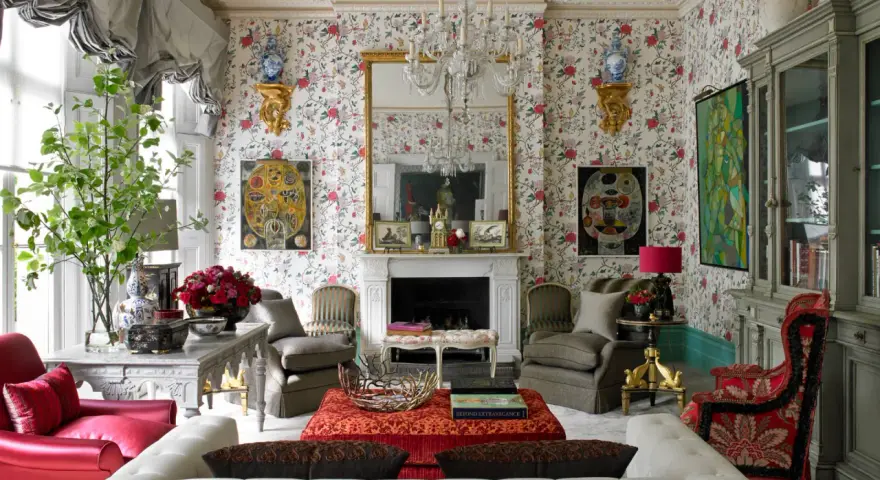 Maximalism inredning med blommig tapet, kristallkrona, röda och grå möbler samt konstverk.