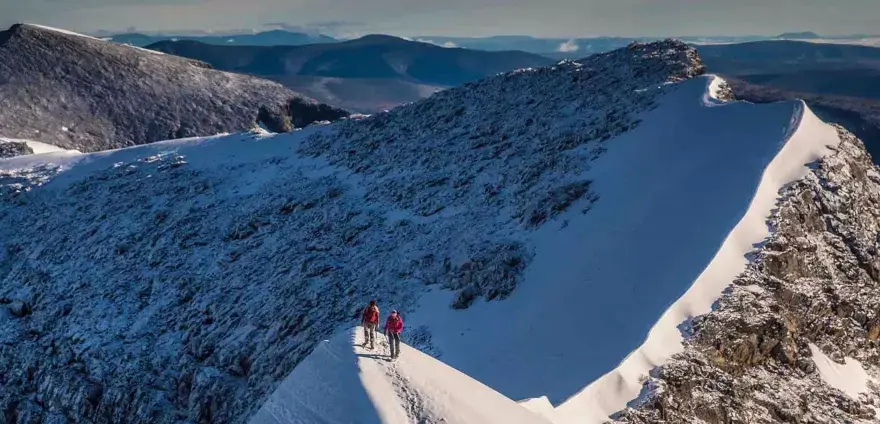 Två vandrare på en snöig bergskam, redo att bestiga Kebnekaise. Vacker utsikt över fjällen.