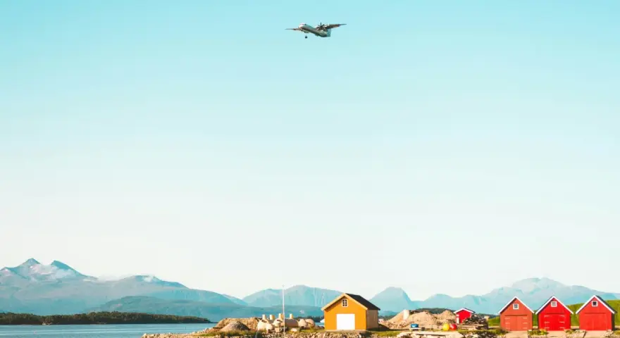 Ett flygplan närmar sig landning vid Molde, Norge. Röda och gula bodar står vid vattnet med berg i bakgrunden.