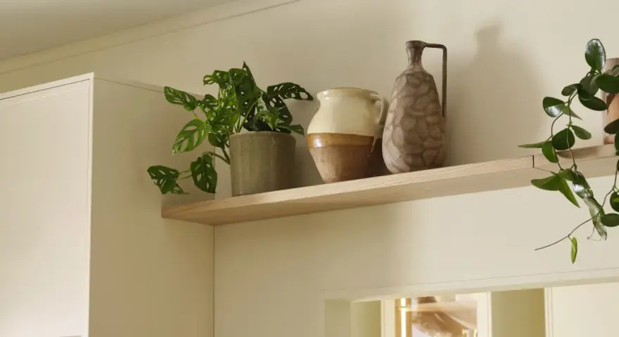 Hylla med krukväxt och två vaser i olika stilar. En beige och brun keramikvas samt en brun, mönstrad vas.