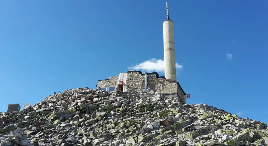 Stone building with a tall tower on a rocky mountain peak under a blue sky.