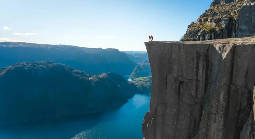 Två personer står på kanten av en klippa med utsikt över Stavangerfjorden.