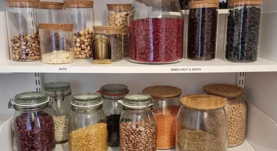 Snyggt organiserat skafferi med glasburkar fyllda med nötter, torkad frukt, frön och baljväxter. Enkelhet och ordning för att organisera skafferi.