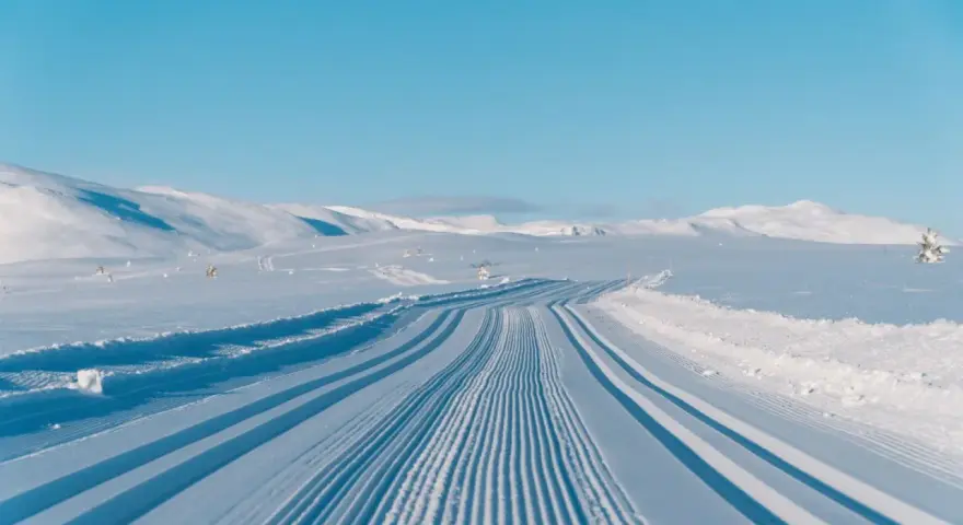 Perfekt preparerade spår för längdskidåkning i Hemsedal. Solen lyser på de snötäckta bergen och den blå himlen.