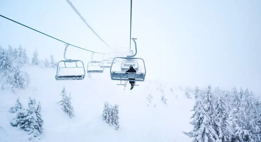 En skidåkare åker linbana uppför ett snötäckt berg i Norge, omgiven av frostiga träd.