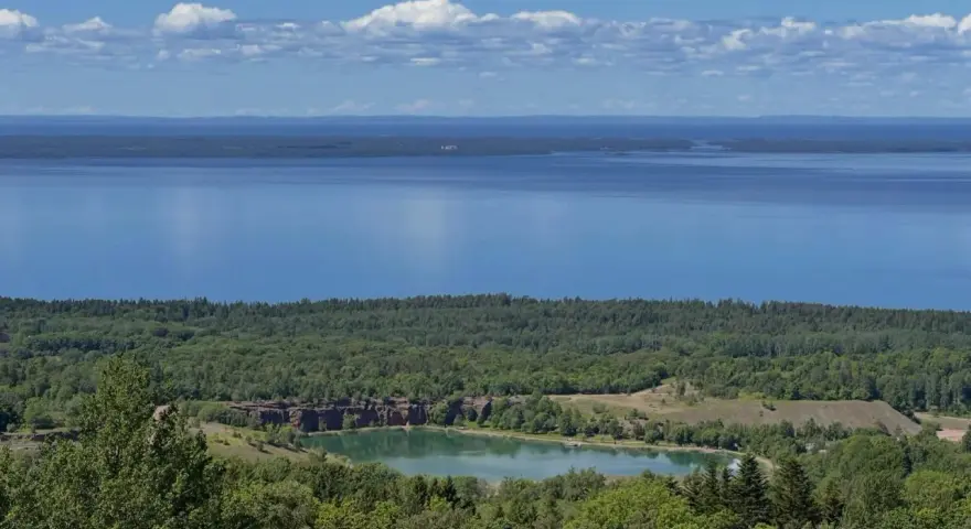 Vacker utsikt över en sjö och en grönskande skog. En liten sjö med klippor syns i mitten, en del av **Götaleden etapp 7**.