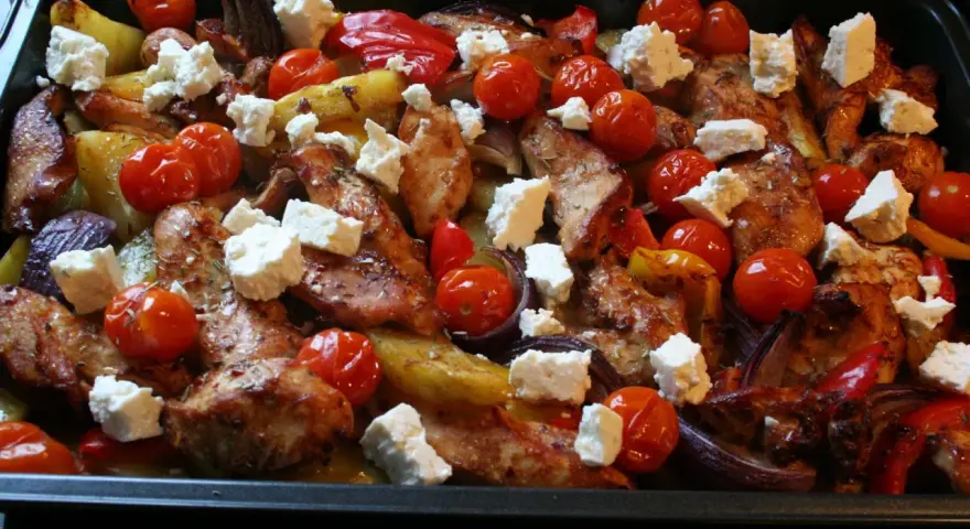 En härlig grekisk pyttipanna med kyckling, potatis, tomater, paprika och fetaost i en ugnsform.