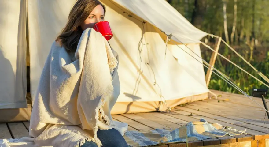 Kvinna med filt och röd mugg vid tältet. En perfekt packlista camping-morgon.
