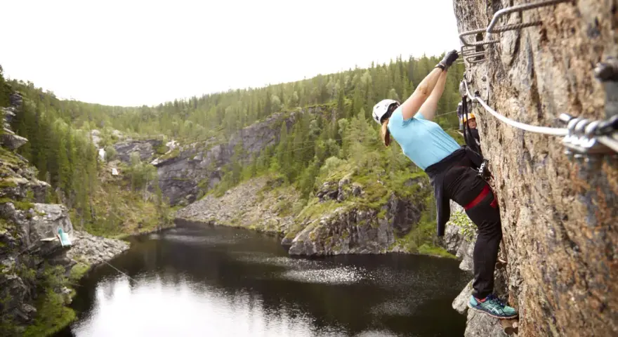 En person klättrar på en klippa vid rypetoppen adventurepark. Vacker natur med sjö och skog.