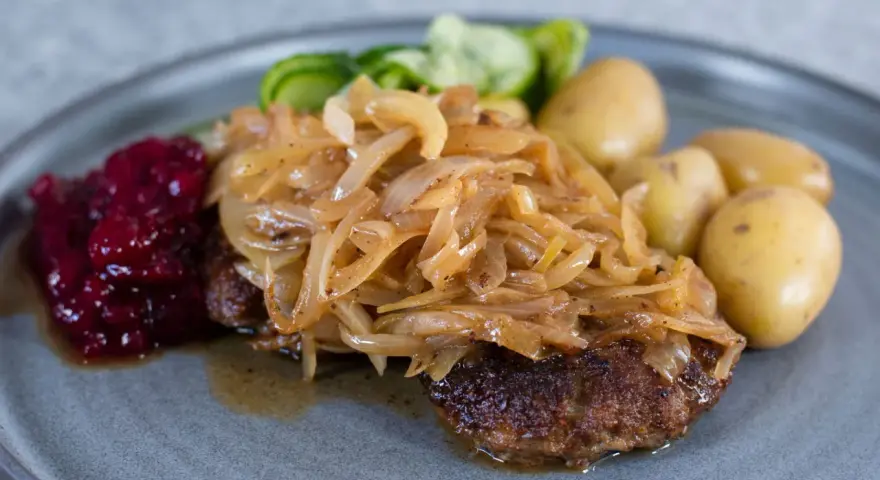 En tallrik med pannbiff, stekt lök, lingonsylt och kokt potatis. Ett klassiskt svenskt pannbiff recept som är lätt att lyckas med.