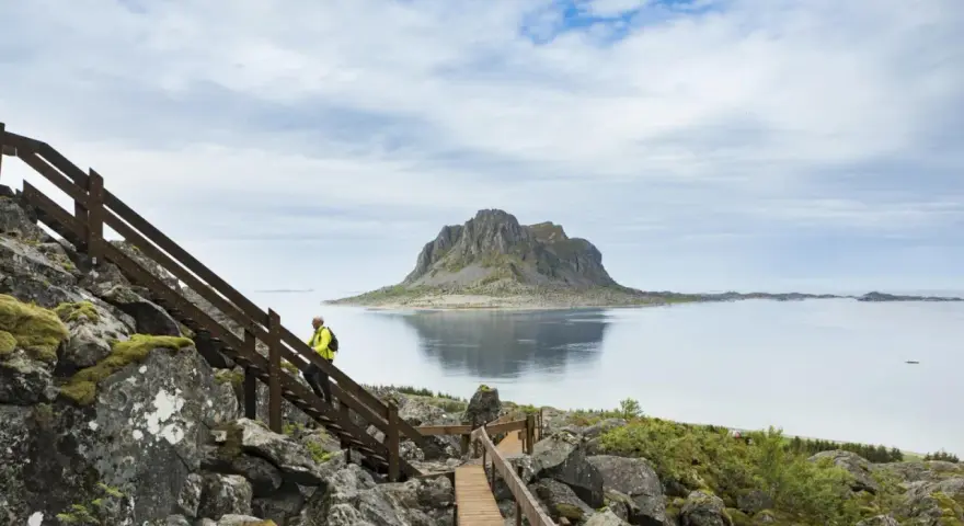 Vandrare på trappor vid havet med en imponerande bergstopp i bakgrunden, en vy från Vega Norge.