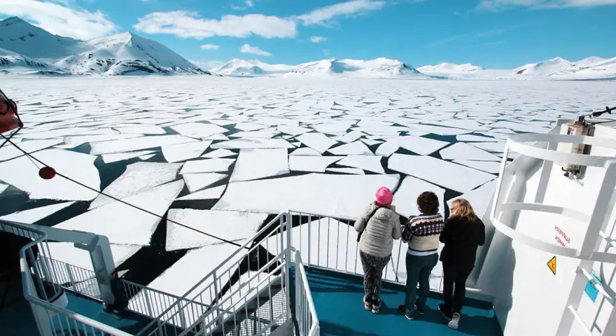 Besök Svalbard och se isflak som bryts upp i ett arktiskt landskap. Tre personer står på ett fartyg och blickar ut över det frusna havet.