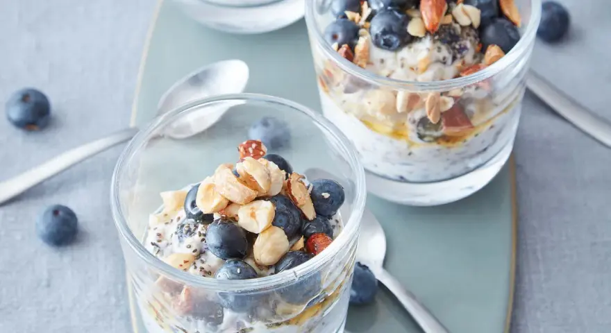 Två glas med overnight oats, toppade med blåbär, nötter och honung. Perfekt frukost!