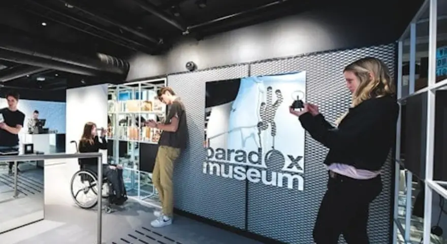 Besökare utforskar utställningar på Paradox Museum Oslo. En kvinna i rullstol tittar på sin telefon.
