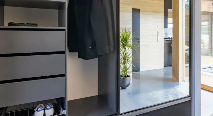 Snygga inredningstips hall: mörk garderob med rockar, mössor, skor och en grön växt som speglas i en stor glasdörr.