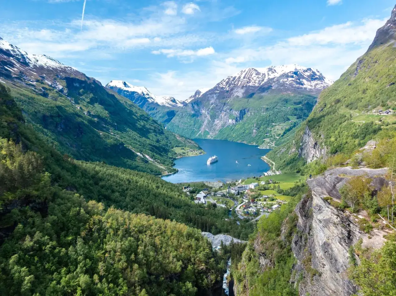 Majestätisk fjord i Norge, med snöklädda berg, grönskande sluttningar och ett kryssningsfartyg i det blå vattnet. En vy som påminner om den vackra naturen vid Bærum, Norge.