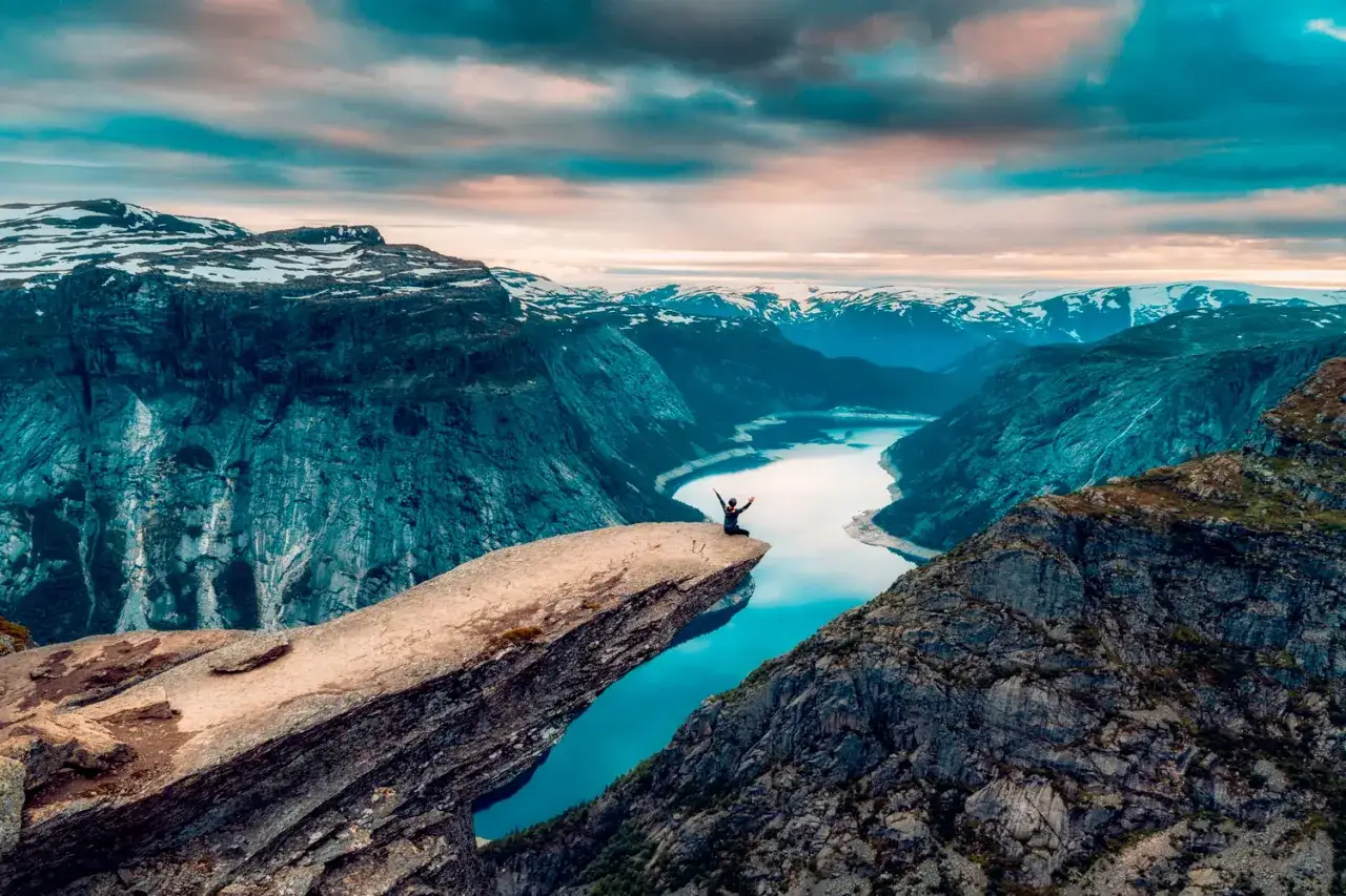 En person firar p&aring; Trolltunga, en ikonisk klippavsats i Norge, med en hisnande utsikt &ouml;ver Innerdalen.