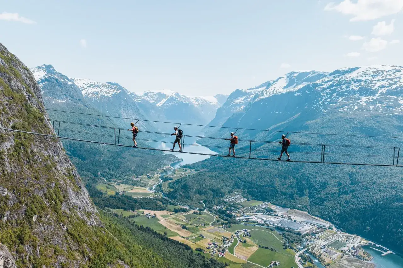 &Auml;ventyrare g&aring;r p&aring; Loen via ferrata, en h&auml;ngbro h&ouml;gt &ouml;ver en dal med sn&ouml;kl&auml;dda berg i bakgrunden.