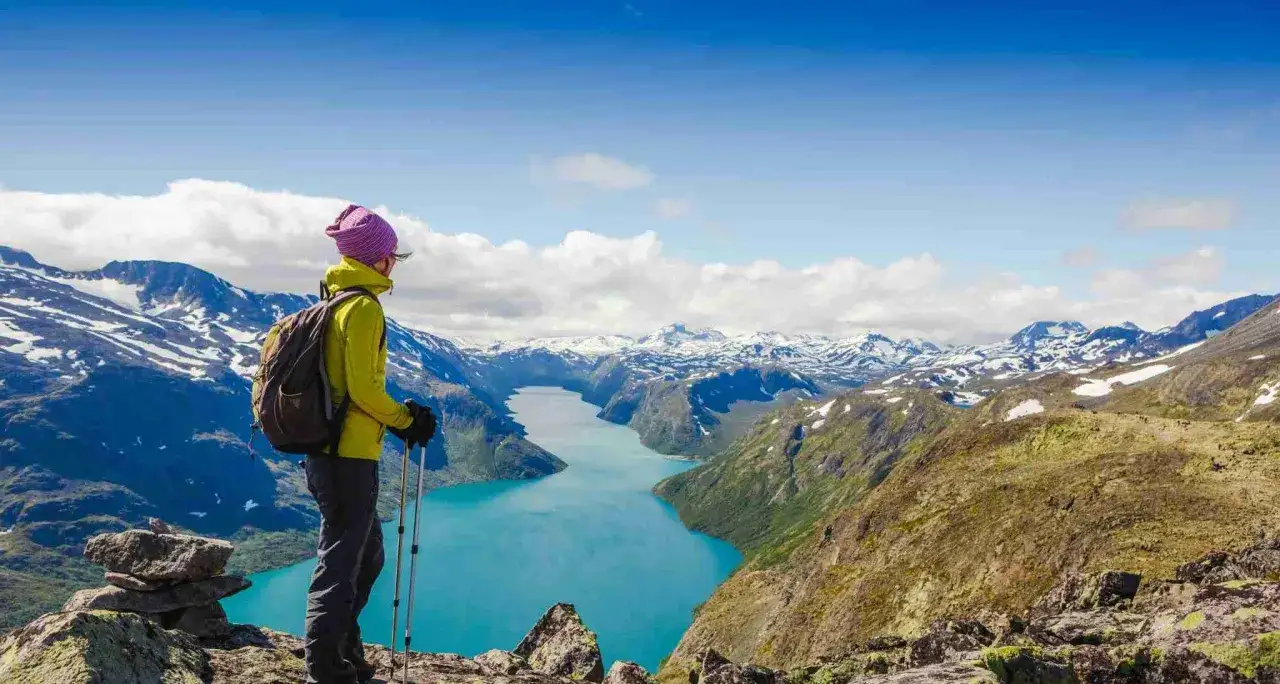 Vandrare njuter av den hisnande utsikten över en turkos sjö och snöklädda berg i Jotunheimen nationalpark.