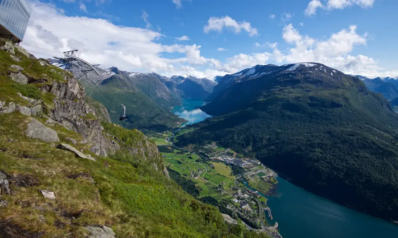 Vy från Loen Norge med linbana som svävar över en djup fjord och gröna berg.