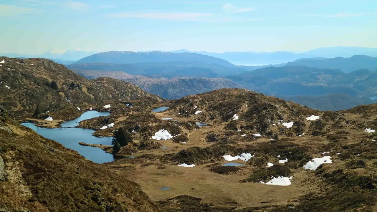Vacker utsikt &ouml;ver Ulriken i Bergen med sm&aring; sj&ouml;ar och sn&ouml;fl&auml;ckar p&aring; bergssluttningarna.