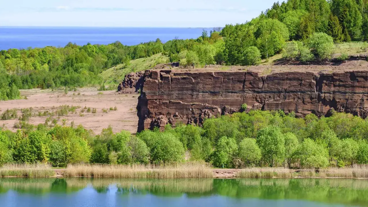Vacker utsikt &ouml;ver en sj&ouml; med vass, en brant klippa och gr&ouml;nskande tr&auml;d. Perfekt f&ouml;r att utforska vandringsleder Kinnekulle karta.