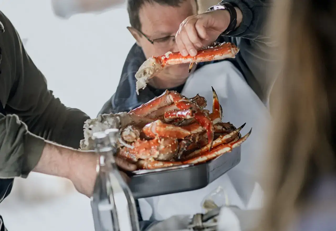 En man visar upp en stor kungskrabba fr&aring;n Norge. Den &auml;r tillagad och serveras i en form.