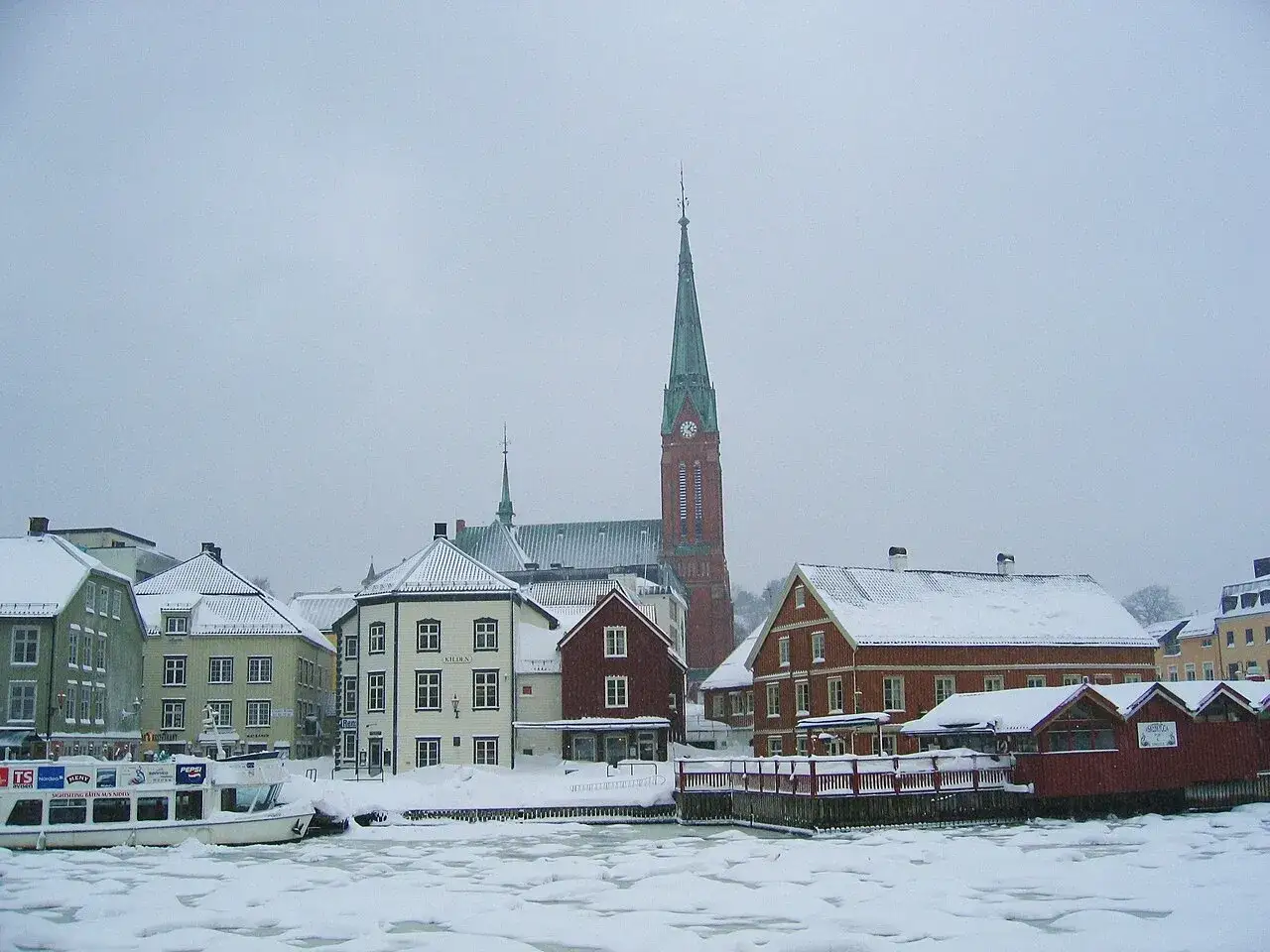 Vintervy över Arendal Norge med snöklädda tak och en kyrka med högt torn. Is på vattnet.