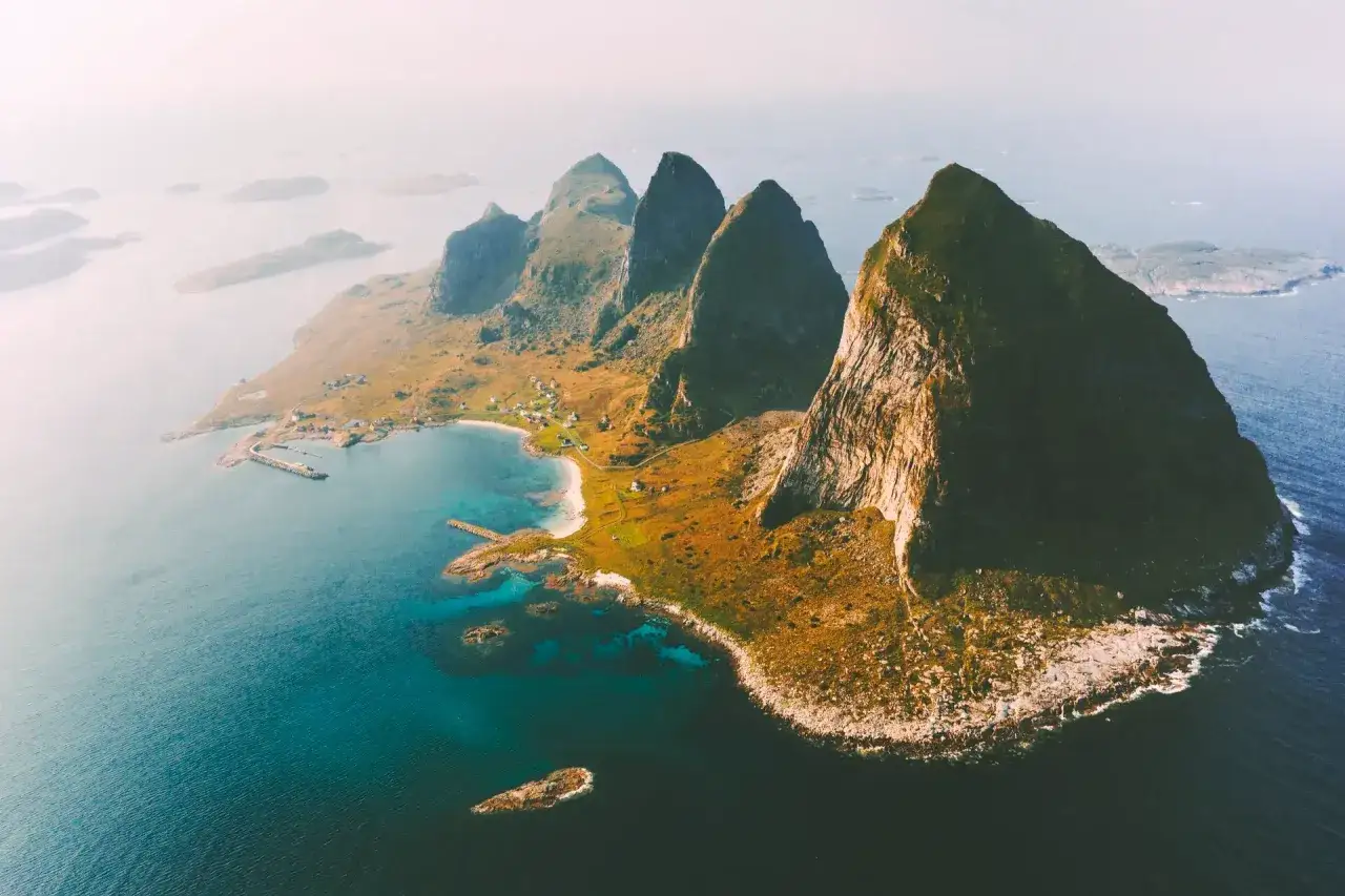 En dramatisk kustlinje med spetsiga berg och en liten by vid havet. En idyllisk plats att tr&auml;na Norge p&aring;, med frisk luft och hisnande vyer.