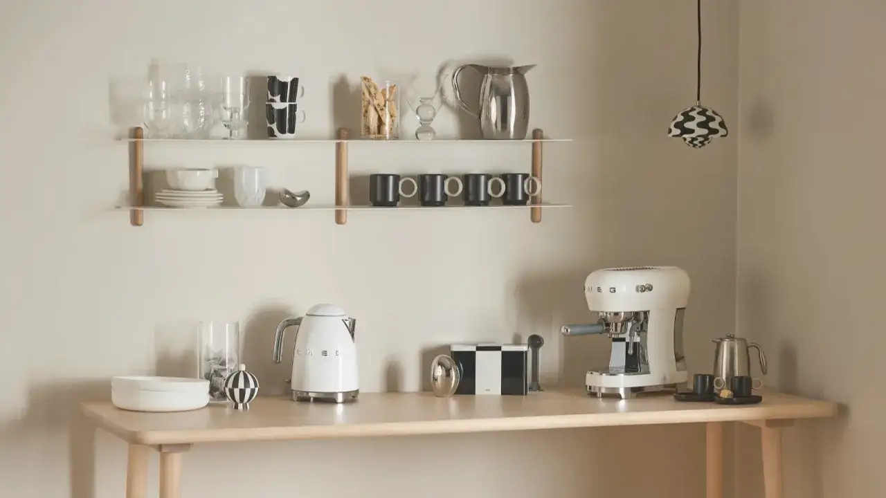 En stilren kaffestation hemma med vit espressomaskin, vattenkokare och muggar på hyllor.