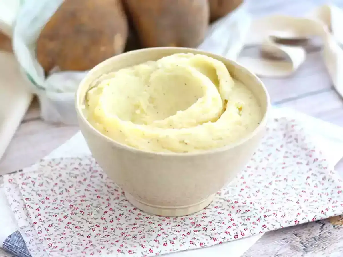 Kr&auml;mig potatismos i sk&aring;l, perfekt f&ouml;r ett enkelt potatismos recept. Bakom skymtar r&aring;a potatisar.